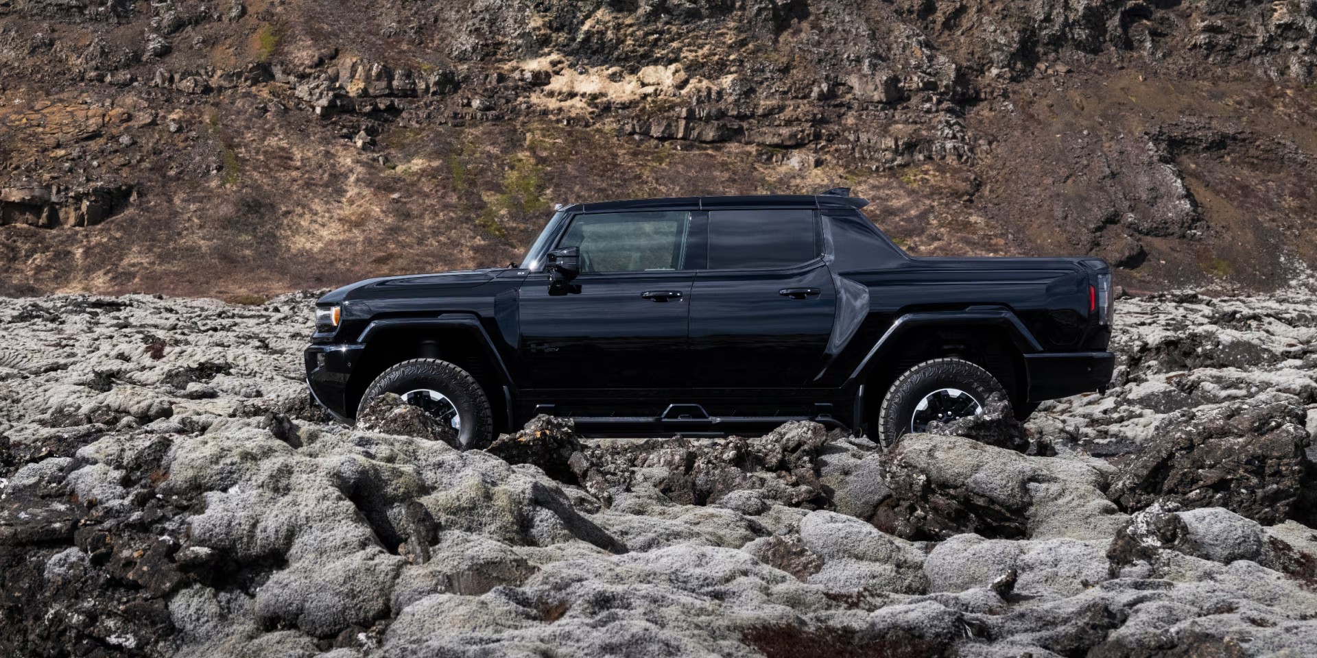 Side view of a black 2025 GMC Hummer EV Pickup Truck parked in the rocky mountains.
