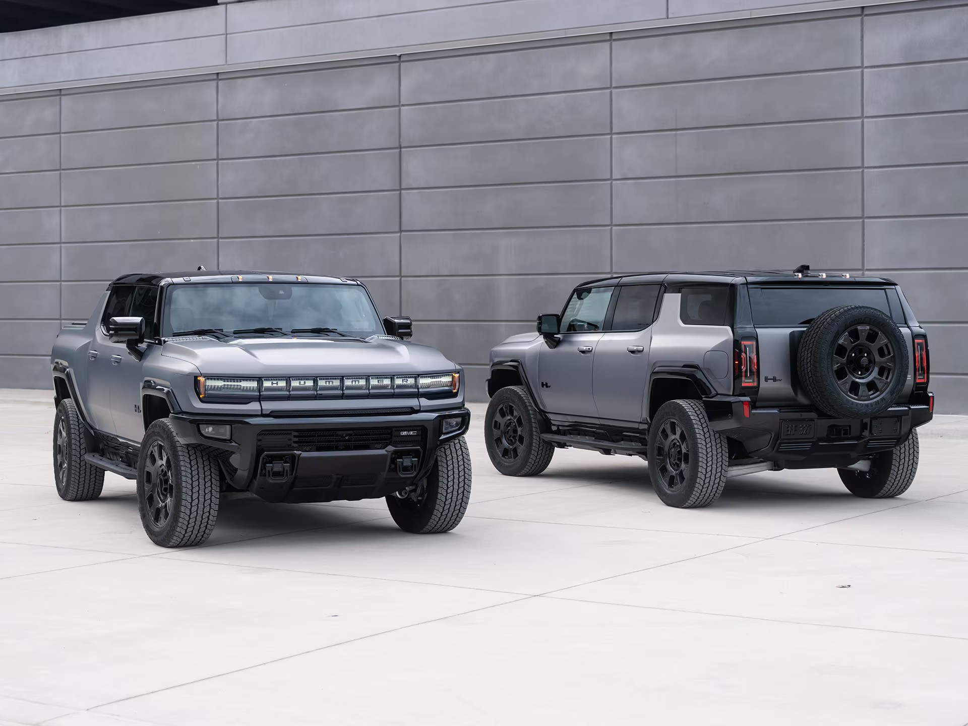 Two 2026 GMC Hummer EVs parked near a wall.
