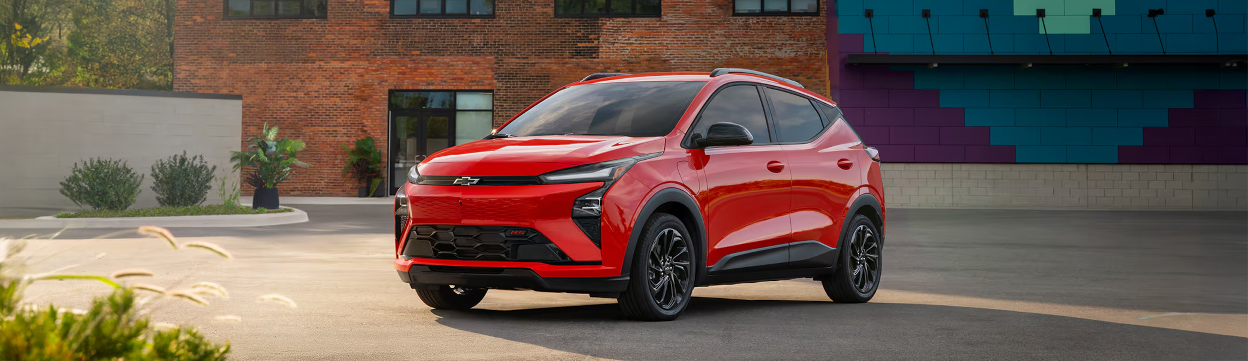 An Orange 2027 Chevrolet Bolt is Parked in Front of a Brown Brick Building