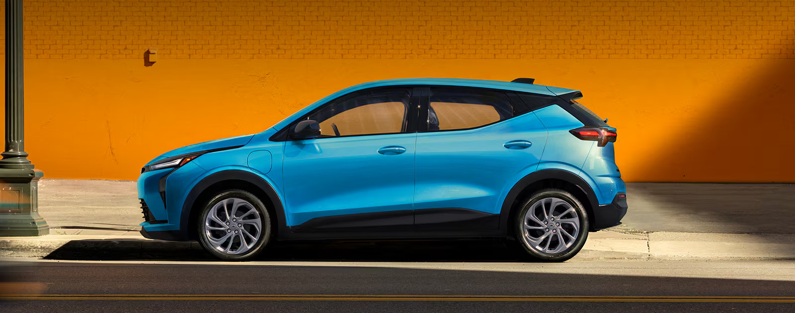 A Light Blue 2027 Chevrolet Bolt is Shown in a Side Profile View, with the Text "Bolt Gets Bolder," and Highlights of its New Front and Rear Fascia, 17" Aluminum Wheels, and Gloss Black Outside Mirrors.