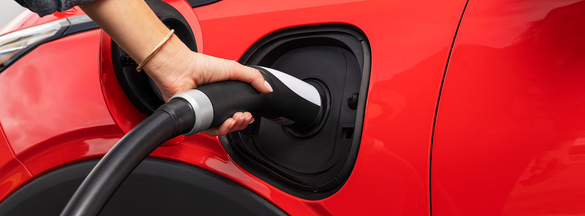 A Close-Up of a Hand Plugging a Charging Cable into the Charging Port of a Red 2027 Chevrolet Bolt.